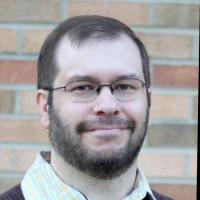 A fair-skinned man with close-cropped light brown hair and a beard and mustache. He is wearing glasses.