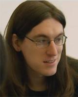 A fair-skinned woman with long dark hair and glasses looks to her right.